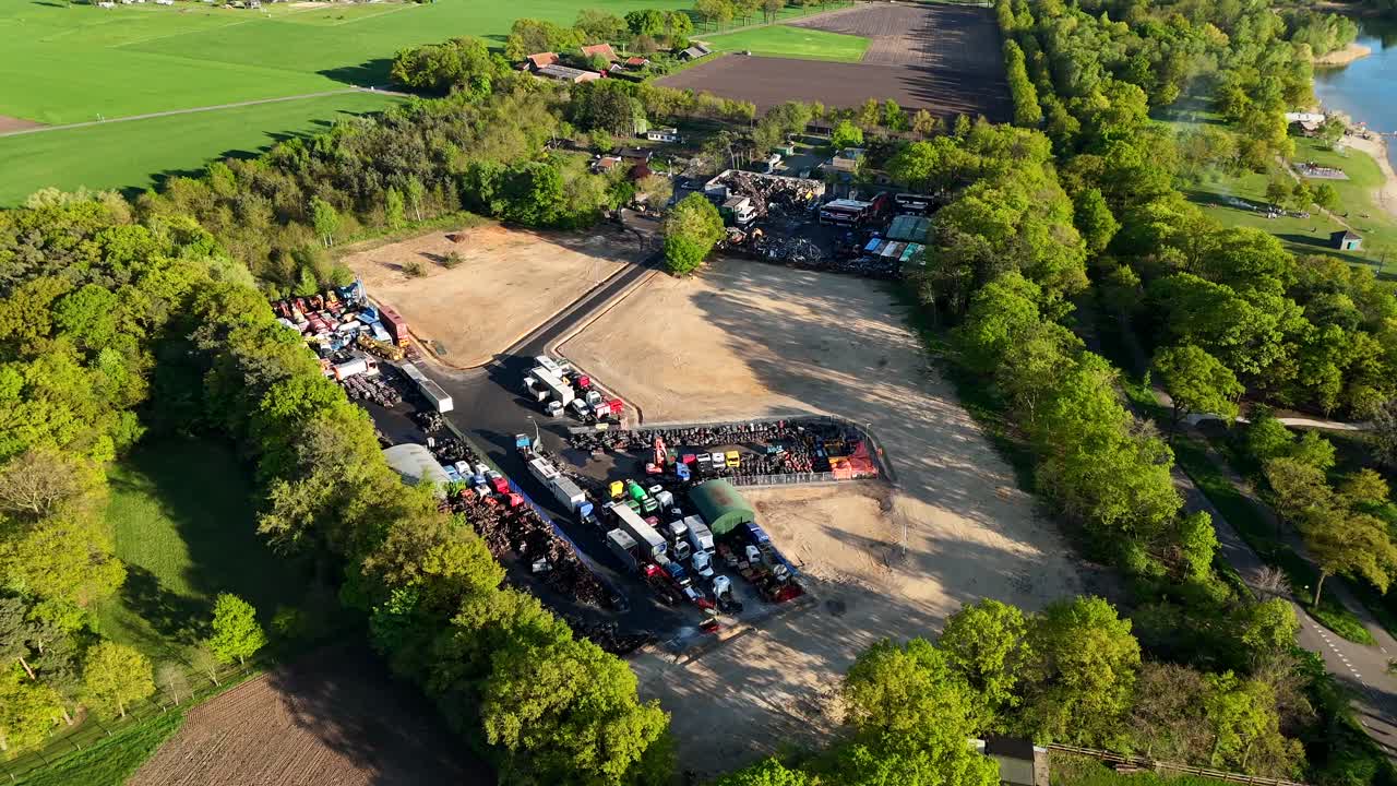 Industrial junkyard field in rural american countryside near lake. Sunset time in usa. Aerial top down flyover. Green trees lighting in the evening. Parking destroyed cars and trucks in suburb.