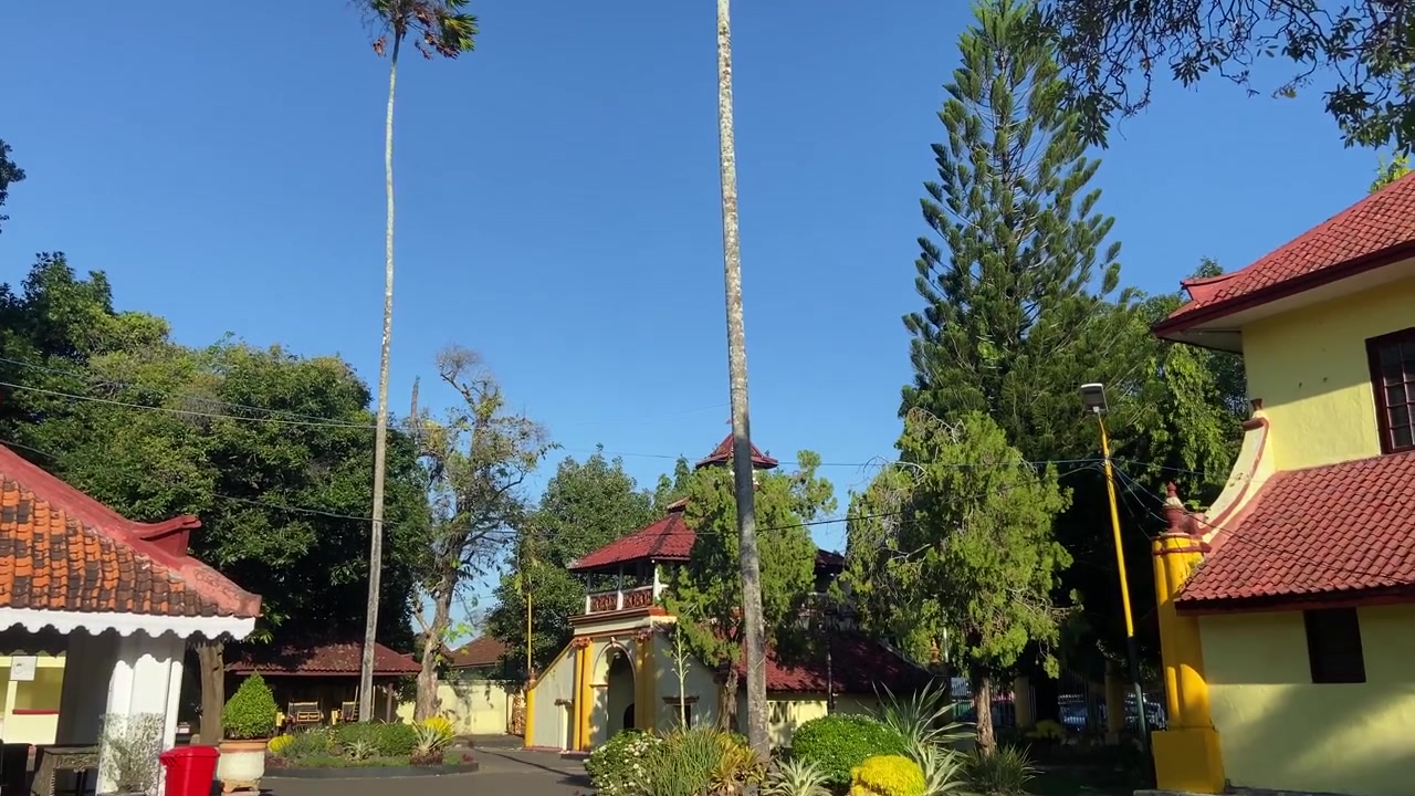 Taman Tropis dengan Bangunan Tradisional dan Pohon Palem Tinggi
