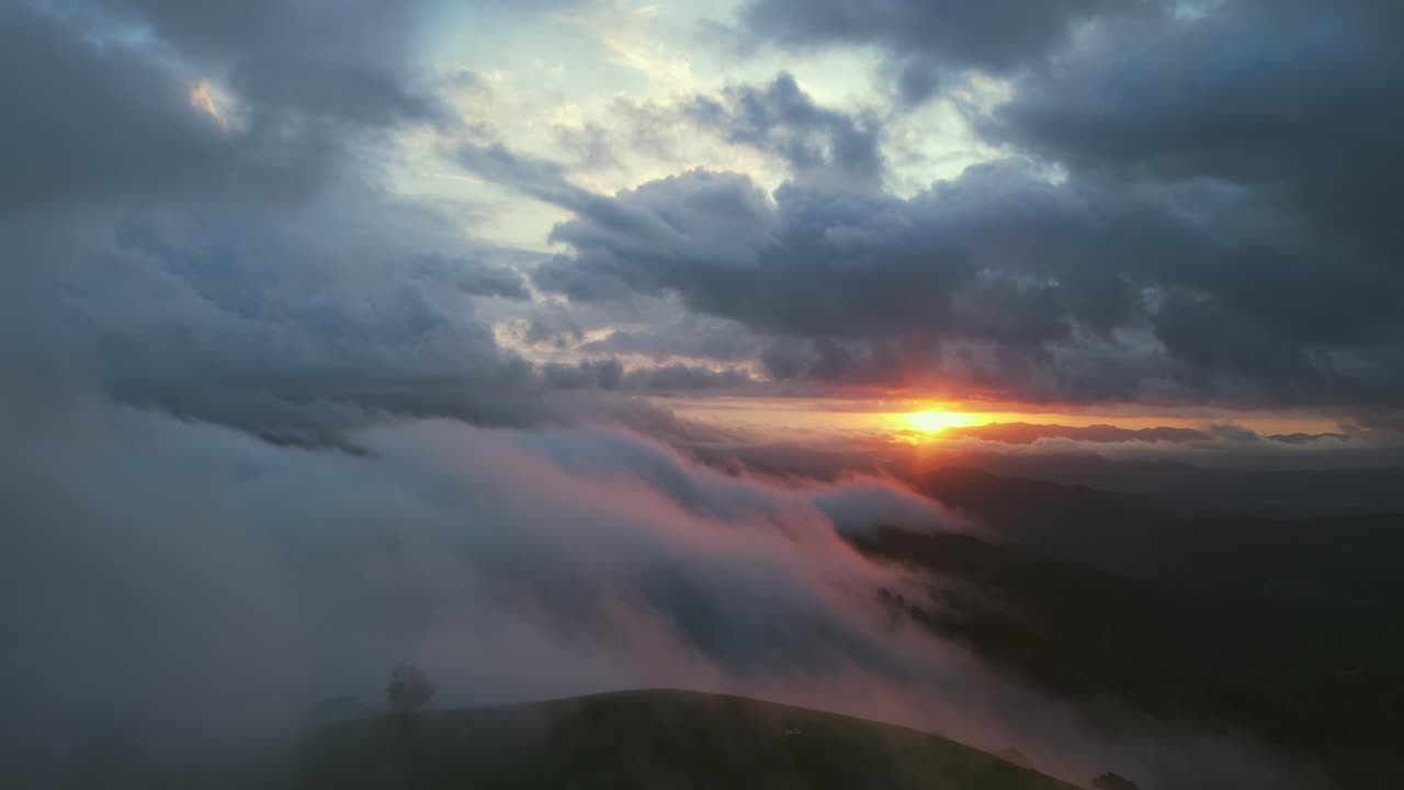 vuelo de drones sobre nubes de niebla con sol naranja brillante al atardecer, 4k