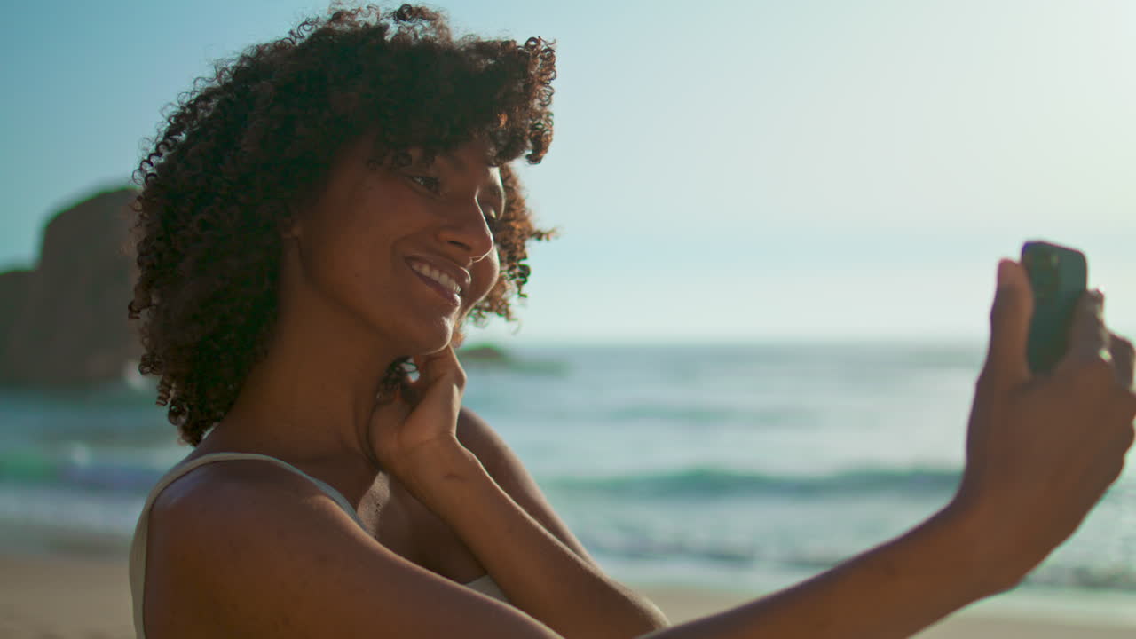 Ragazza sorridente che si fa un selfie posando in spiaggia in primo piano. Donna in ritratto verticale.