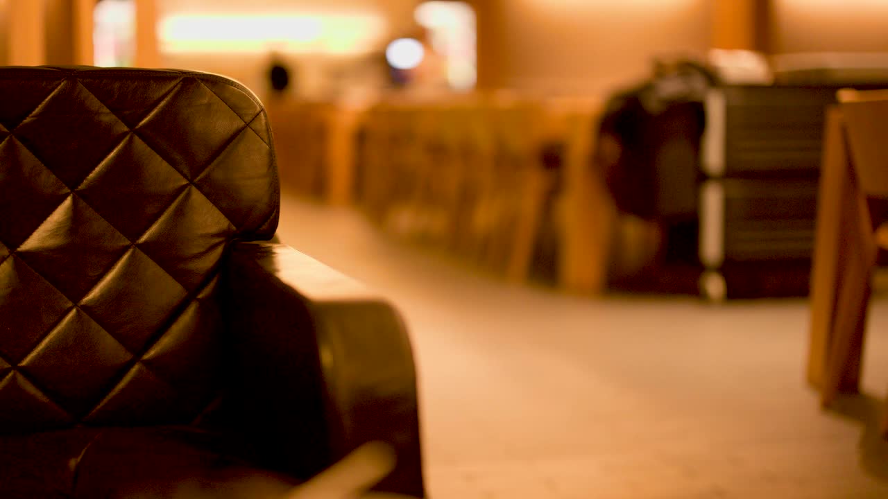 Camera slowly moves toward empty leather chair in warmly lit, modern airport lounge interior