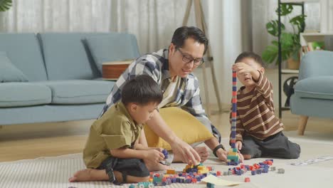 full body of asian father and sons assemble the construction set colorful plastic toy brick on a mat at home