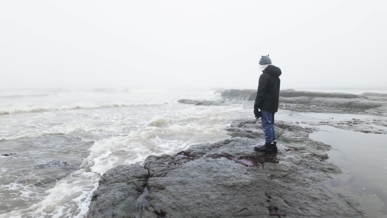 niño de pie en las rocas en un paisaje costero