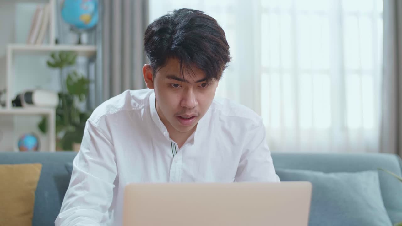 Happy Asian Man Celebrating While Using Laptop Computer In The Living Room