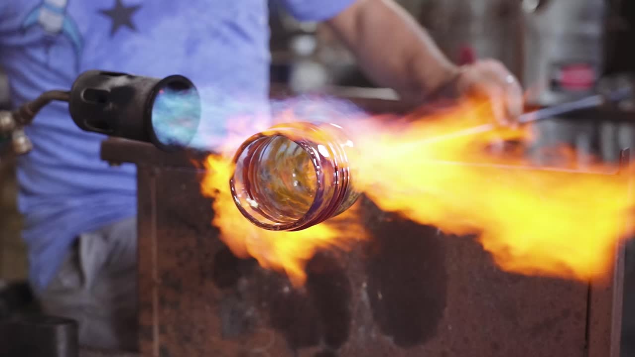 Un soffiatore di vetro che riscalda un bicchiere da whisky con fiamme.