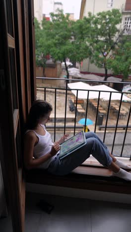 young woman working on a tablet on a balcony on a rainy day