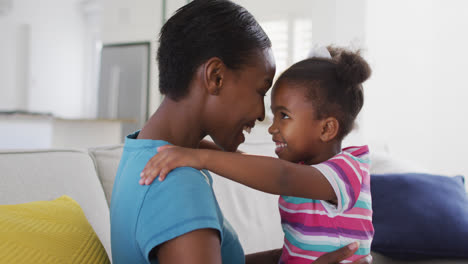 Happy-african-american-mother-and-daughter-sitting-on-sofa-and-touching-foreheads