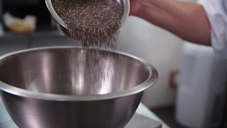 Chia-seeds-poured-by-a-female-chef,-from-a-small-metallic-bowl-in-to-a-large-bowl