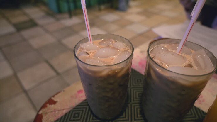 A row of delicious blended iced coffee frappes and chocolate shakes topped with foam, served in tall glasses with straws on a modern cafe counter