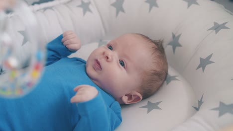 little child looks at rattle in mom hand in sleeping cocoon