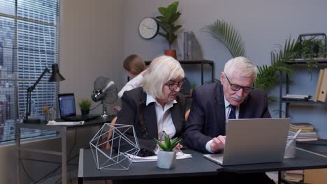 elderly man boss with woman colleague working in office, secretary relaxing with electric fan