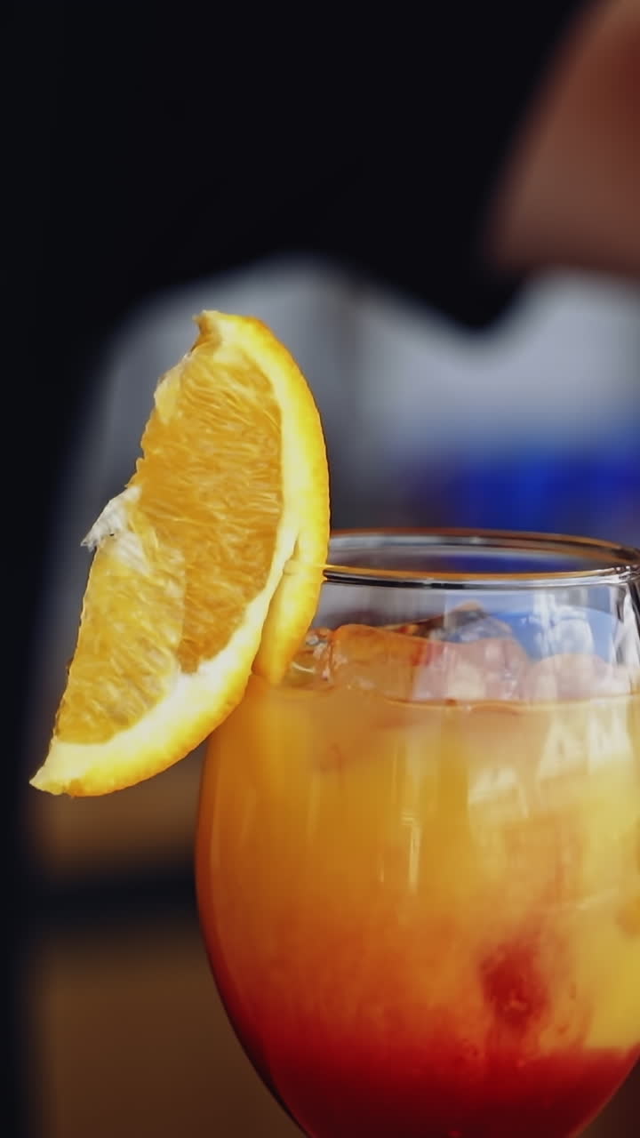 Ready cocktail on a bar table. Bartender puts a slice of orange on the top of the glass with bright beverage. Glass with drink in the nightclub. Vertical video