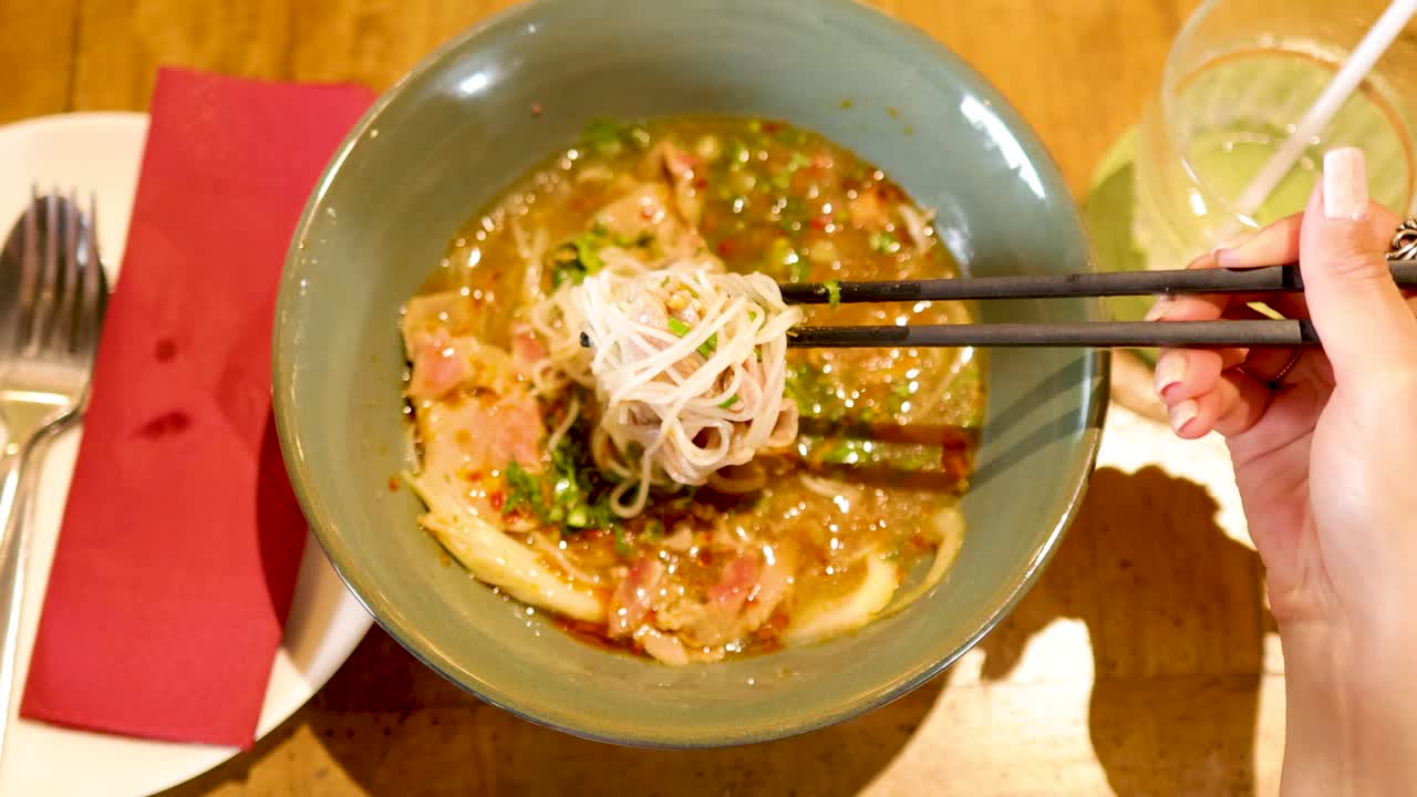 Chopsticks lift noodles from a flavorful Vietnamese dish in a Bangkok restaurant, highlighting vibrant colors and inviting ambiance