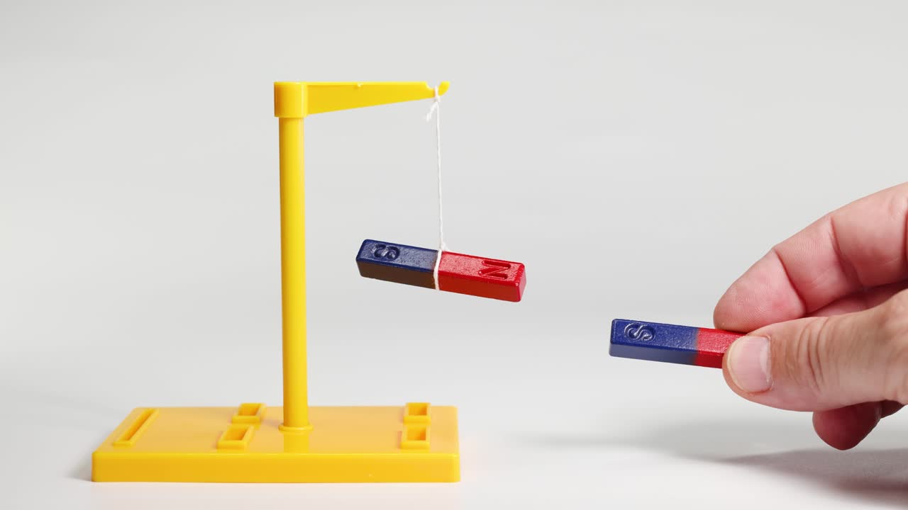 Hands manipulate magnets on a stand, illustrating magnetic attraction and repulsion. Bright lighting highlights the dynamic interaction