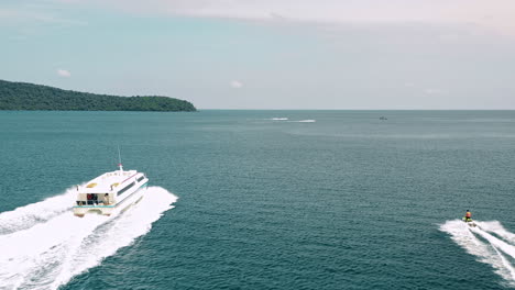 following a large tour boat and jet ski racing across the bay of rong samloem, cambodia, aerial