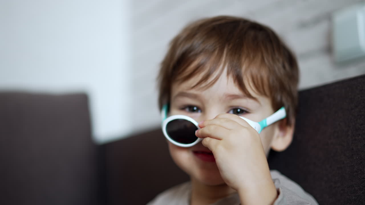 Beautiful Caucasian toddler boy puts off sunglasses and put them on again. Lovely kid portrait close up.