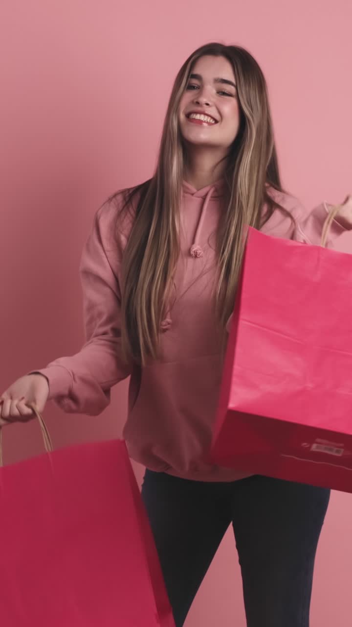 Happy shopaholic woman with shopping bags in pink studio