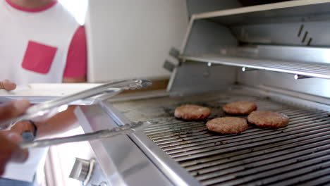 grilling burgers on barbecue grill, person using tongs for flipping patties