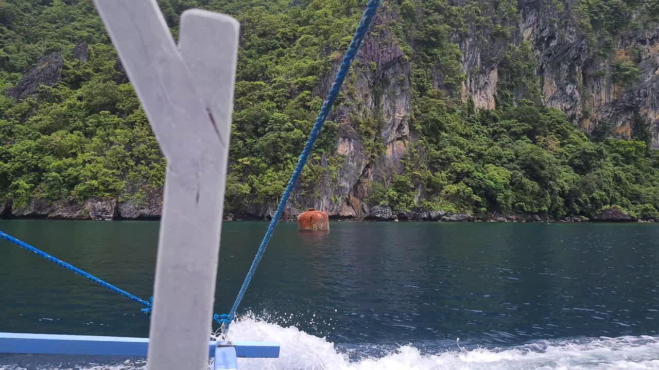 Wooden Filipino Bangka Catamaran Boat Sailing by Uninhabited Island WIth Steep Limestone Cliffs