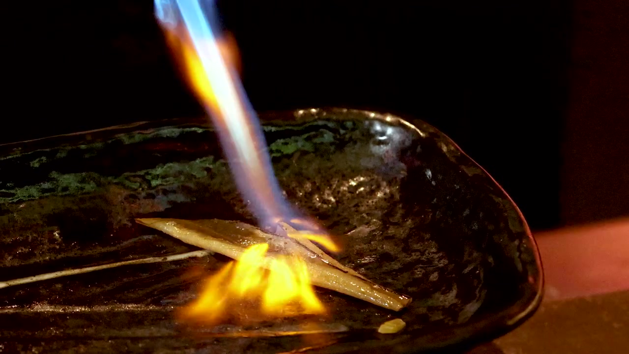 Close-up shot of a chef searing anago eel with a blue blowtorch flame