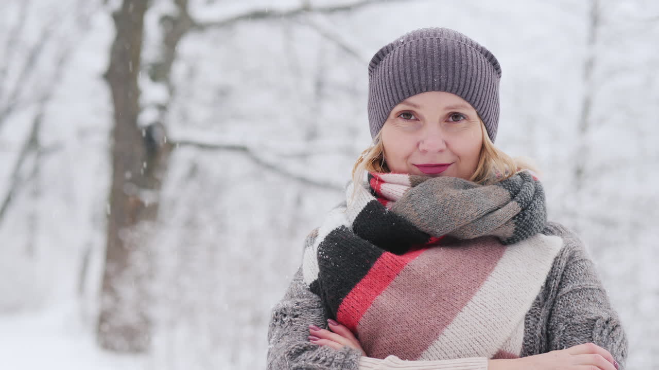 A Woman In A Warm Sweater And A Bright Scarf Stands In A Snow Park