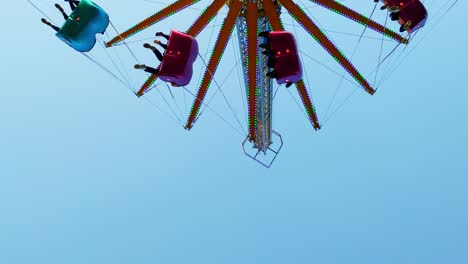 low angle view of colorful chain fair swing spinning people around, minimal background blue sky, static