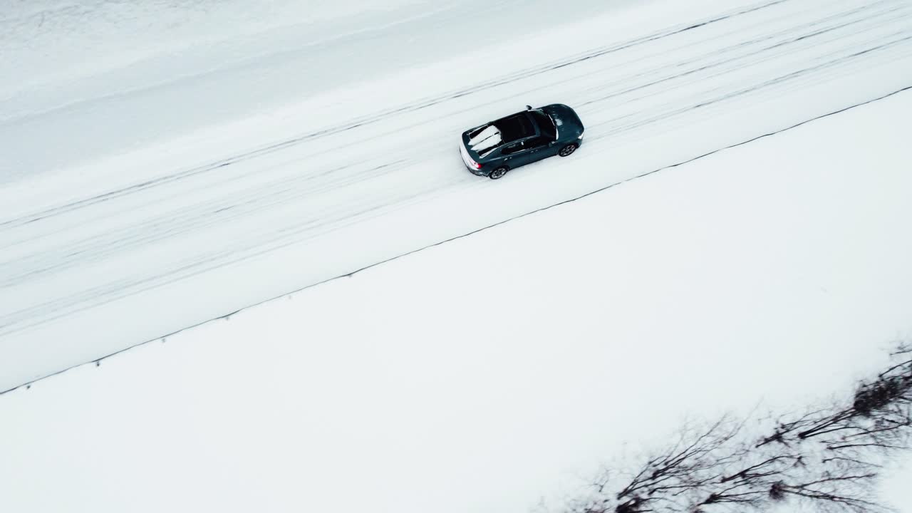 un coche eléctrico está conduciendo por una carretera cubierta de nieve en el círculo ártico durante una nevada, seguido por un avión no tripulado