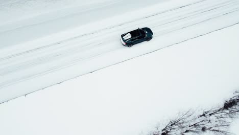 an electric car is driving on a snow-covered road in the arctic circle during a snowfall, followed by a drone