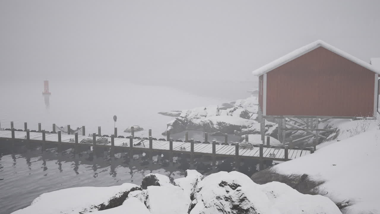 Snowy winter landscape with a dock and red cabin near the water