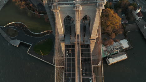 High-angle-view-of-cars-driving-on-Brooklyn-bridge-over-river.-Tilt-up-reveal-of-Suspension-tower-with-US-flag-on-top.-Manhattan,-New-York-City,-USA