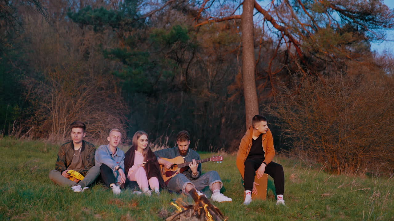 Friends sitting around bonfire. Cheerful friends singing songs and playing guitar near bonfire