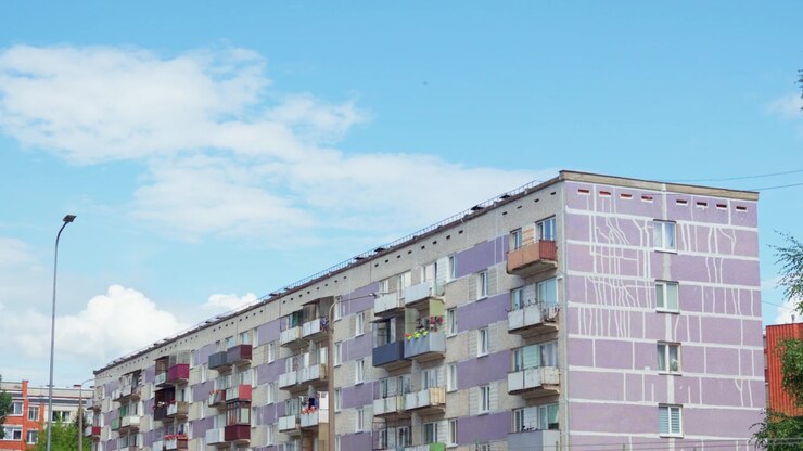 Inquadratura inclinata dal basso che guarda in alto un edificio residenziale a pannelli in stile sovietico sotto un cielo blu con nuvole leggere nel distretto di Daugavpils, catturando l'architettura urbana baltica.