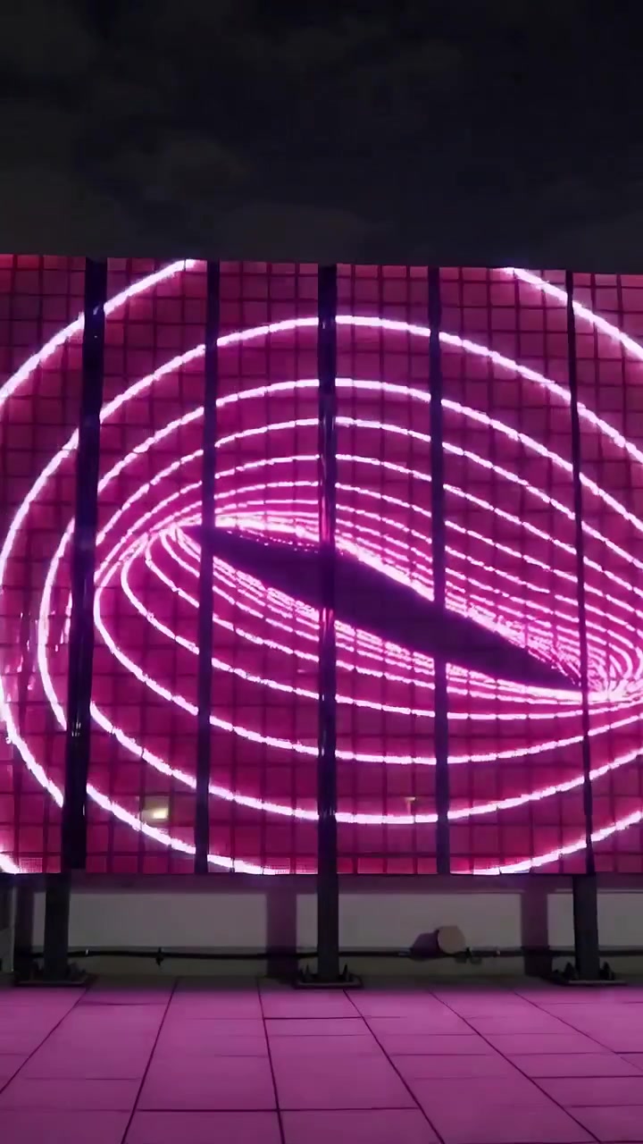 Vídeo vertical: Painel de LED em loop exibindo anéis ovais giratórios no telhado com feixes de luz