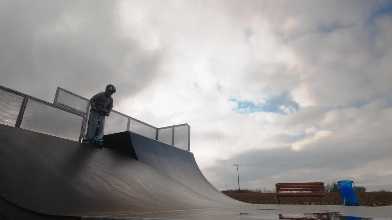 Backlit urban scooter skater descends ramp obstacle in Slow-mo action