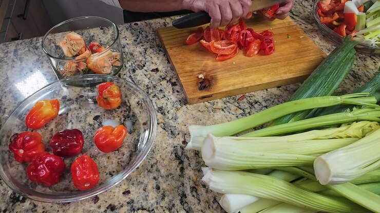 Top view of female hands slicing sweet chili peppers on wooden board