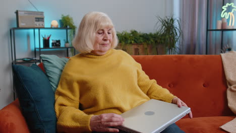 Grandmother-woman-freelancer-on-sofa-closing-laptop-pc-after-finishing-work-in-living-room-at-home