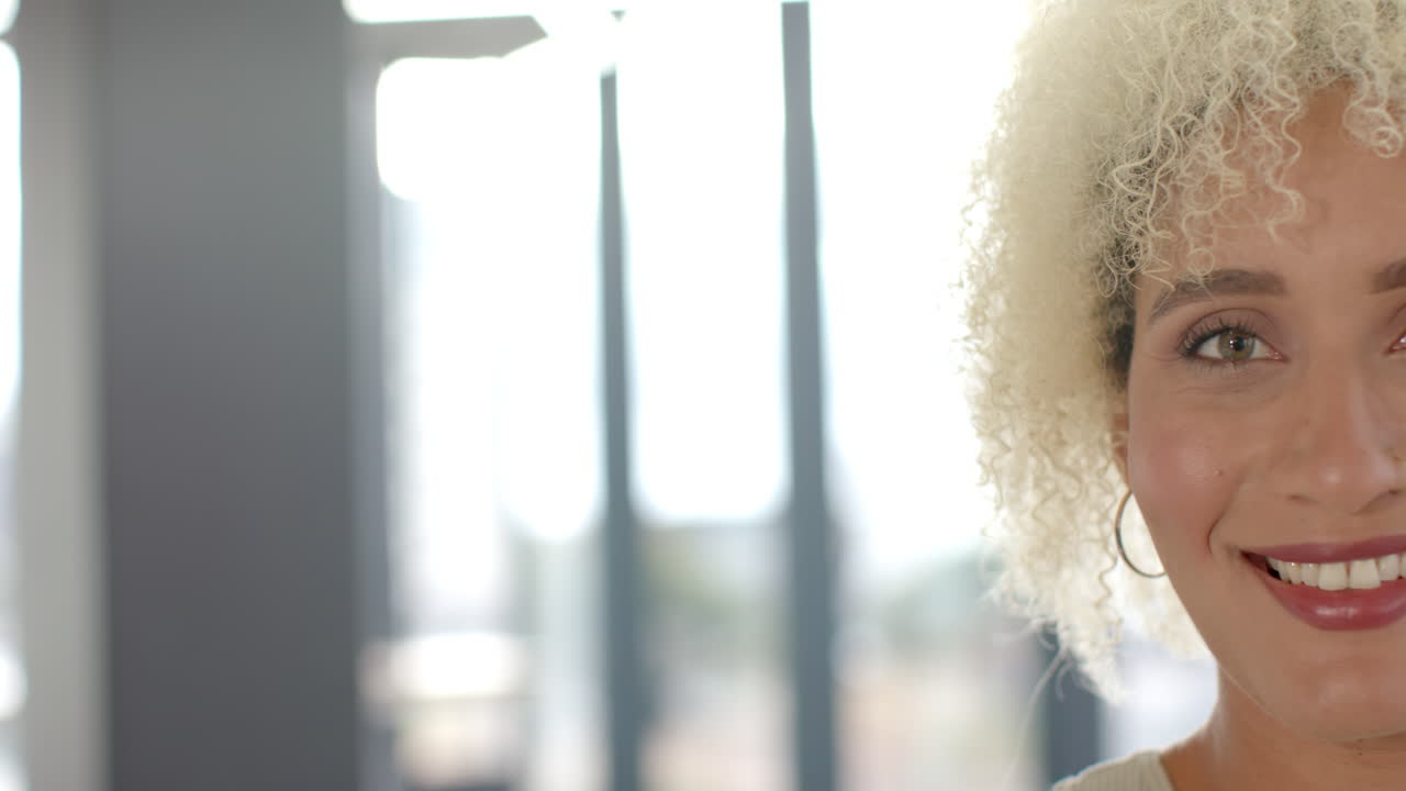 Smiling woman with curly hair wearing hoop earrings in bright office setting, copy space