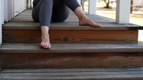 Person sitting barefoot on wooden porch steps