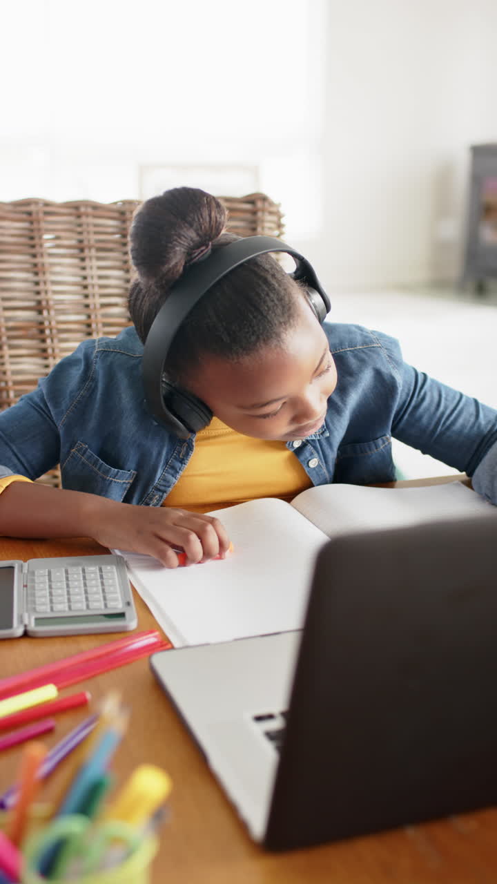Vertical video of happy african american girl using laptop for online lesson, in slow motion