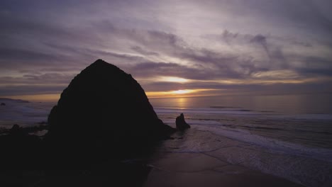 Wide-aerial-rotating-view-around-giant-rock-at-Cannon-Beach-Oregon-Coast-in-USA-during-colourful-peaceful-sunset-dramatic-colours-on-clouds-in-the-sky
