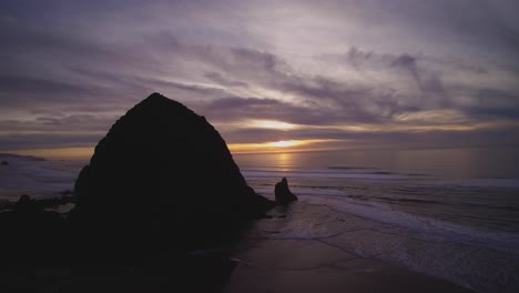 wide aerial rotating view around giant rock at cannon beach oregon coast in usa during colourful peaceful sunset dramatic colours on clouds in the sky