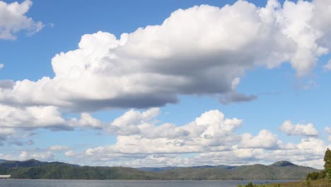 watch fluffy clouds drift across a clear blue sky above lush green hills.