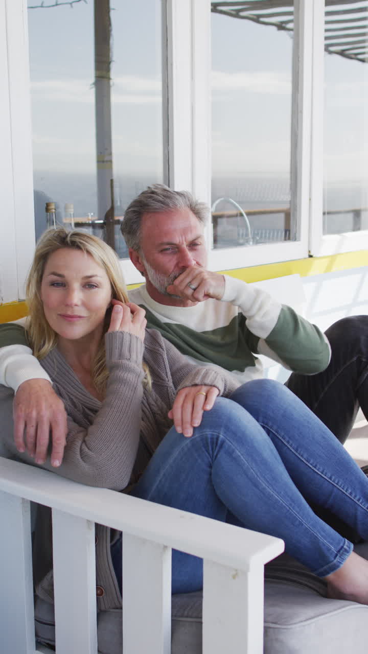 베란다에 있는 소파에 앉아 안고 있는 백인 부부의 수직