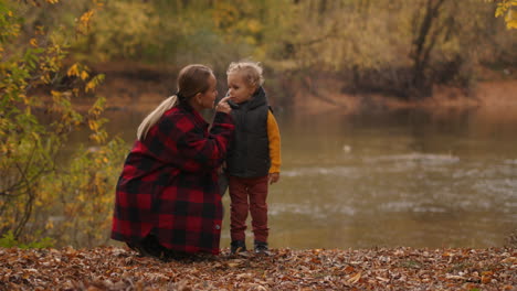 young woman is playing with her toddler in forest resting on shore of lake at autumn day happy family weekend at nature happiness and calmness