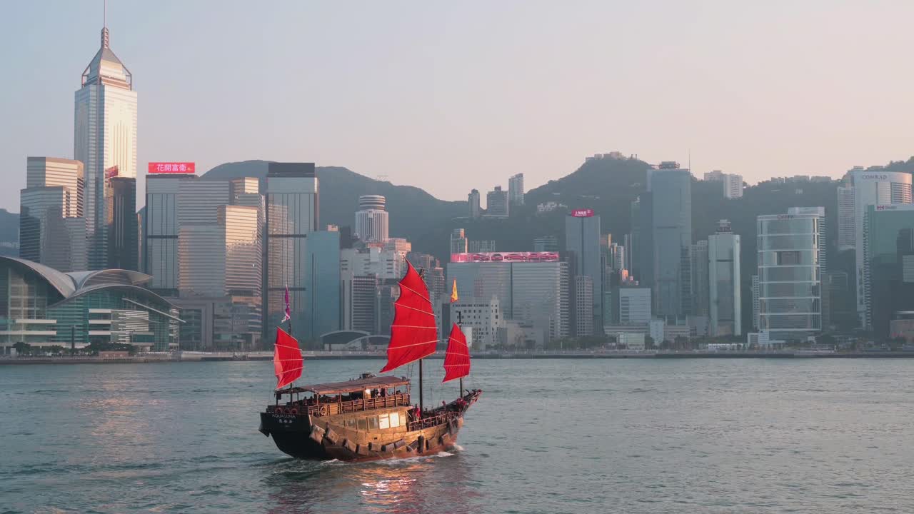 vista de la costa del puerto de victoria como un bote de chatarra de vela roja de madera basado en antiguos veleros chinos, ahora utilizado como atracción turística, navega frente al horizonte de la isla de hong kong