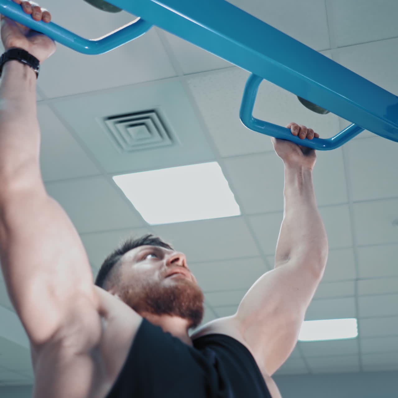 Close-up of concentrated young athlete tightening his body. Strong muscular man exercising fitness training to his arms during workout in the gym.