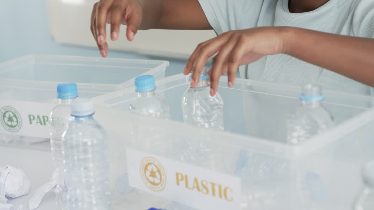 Child is reaching and is sorting bottles on table, is placing into PLASTIC bin for recycling