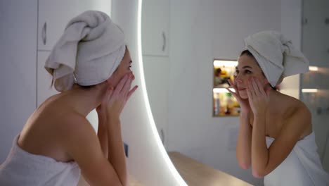 Frau-Im-Bademantel-Berührt-Ihr-Gesicht-Und-Schaut-In-Den-Spiegel-Im-Badezimmer