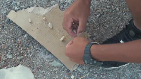 close up shot of a refugee preparing hooks with bait before fishing