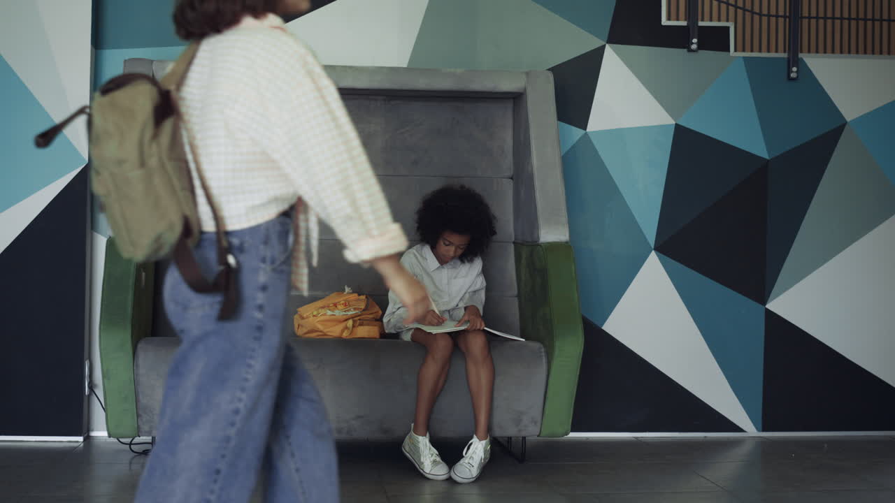 Preteen schoolgirl doing homework in hall. African american girl sitting bench.